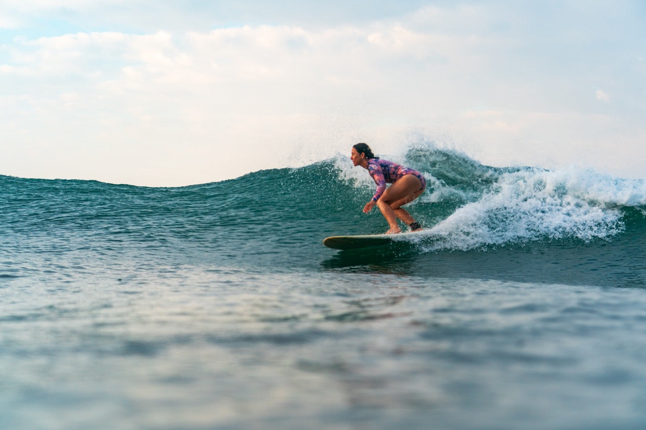 A woman surfs a wave wearing a long sleeve printed swimsuit